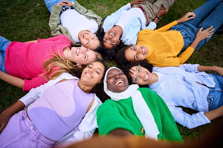 Selfie of multiracial group young female community friends lying in circle on grass looking smiling.