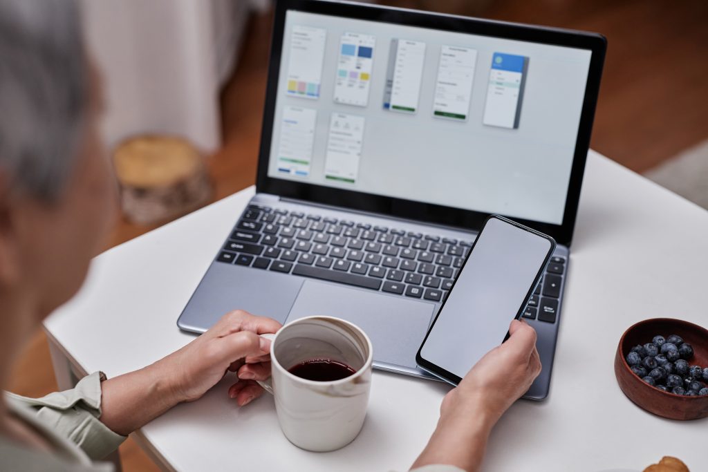 Senior woman using smartphone with blank white screen and laptop